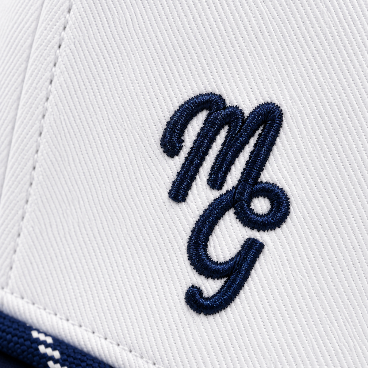 Close-up of a white structured cap featuring an embroidered navy blue cursive 'MGG' logo on the side.