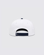 White baseball cap shown from the back, featuring a navy blue adjustable strap with a small white embroidered logo and a navy blue button on top.