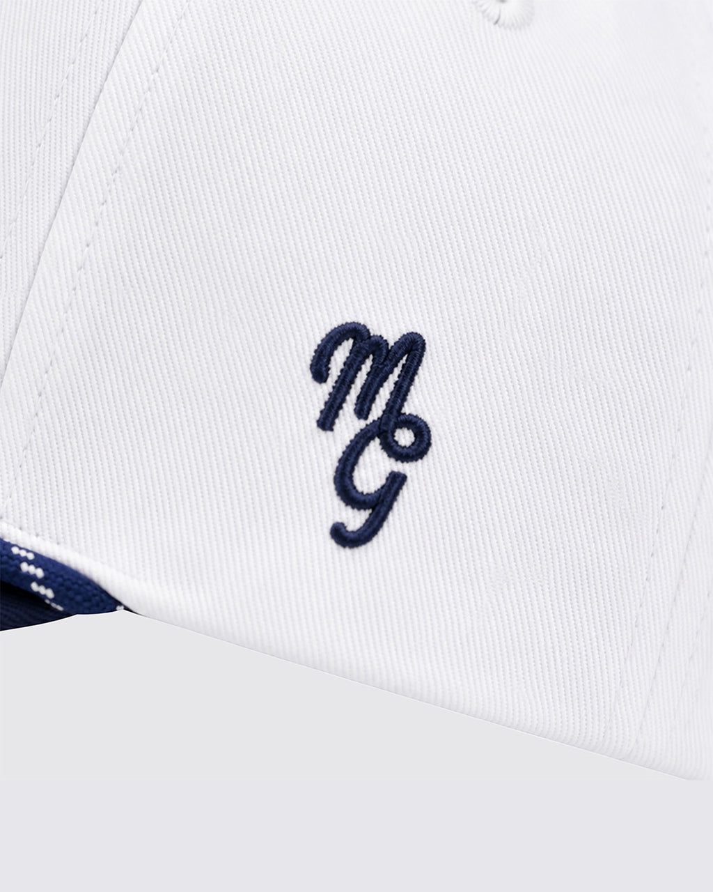 Close-up of a white structured cap with a navy blue embroidered monogram logo on the front panel.