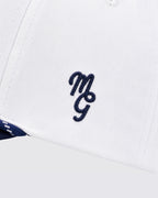 Close-up of a white structured cap with a navy blue embroidered monogram logo on the front panel.